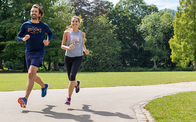 Two runners mid run on a paved path in a park.