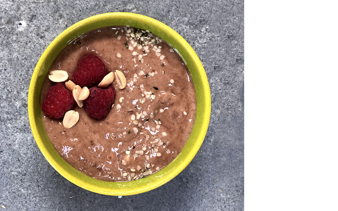 Una imagen desde arriba de una mousse de chocolate y chía con frambuesas, cacahuetes y sirope de arce.