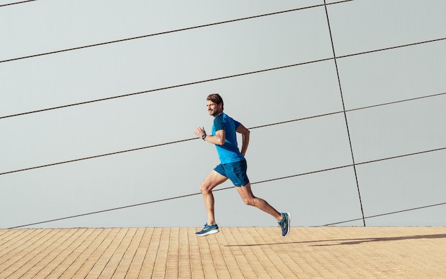 Un runner regarde sur le côté en courant sur un trottoir de la ville.