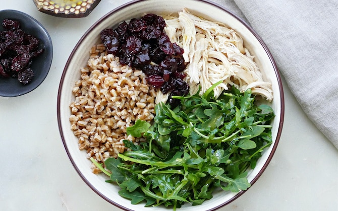 Vista dall’alto di una bowl di farro con pollo, rucola e ciliegie essiccate.