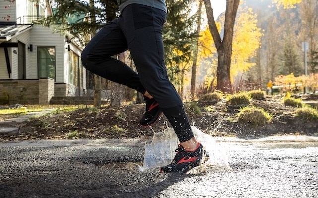 A runner steps in a puddle of water while running in the rain.