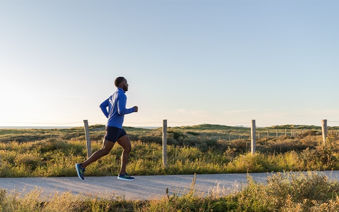 Man runs on a trail through a meadow.